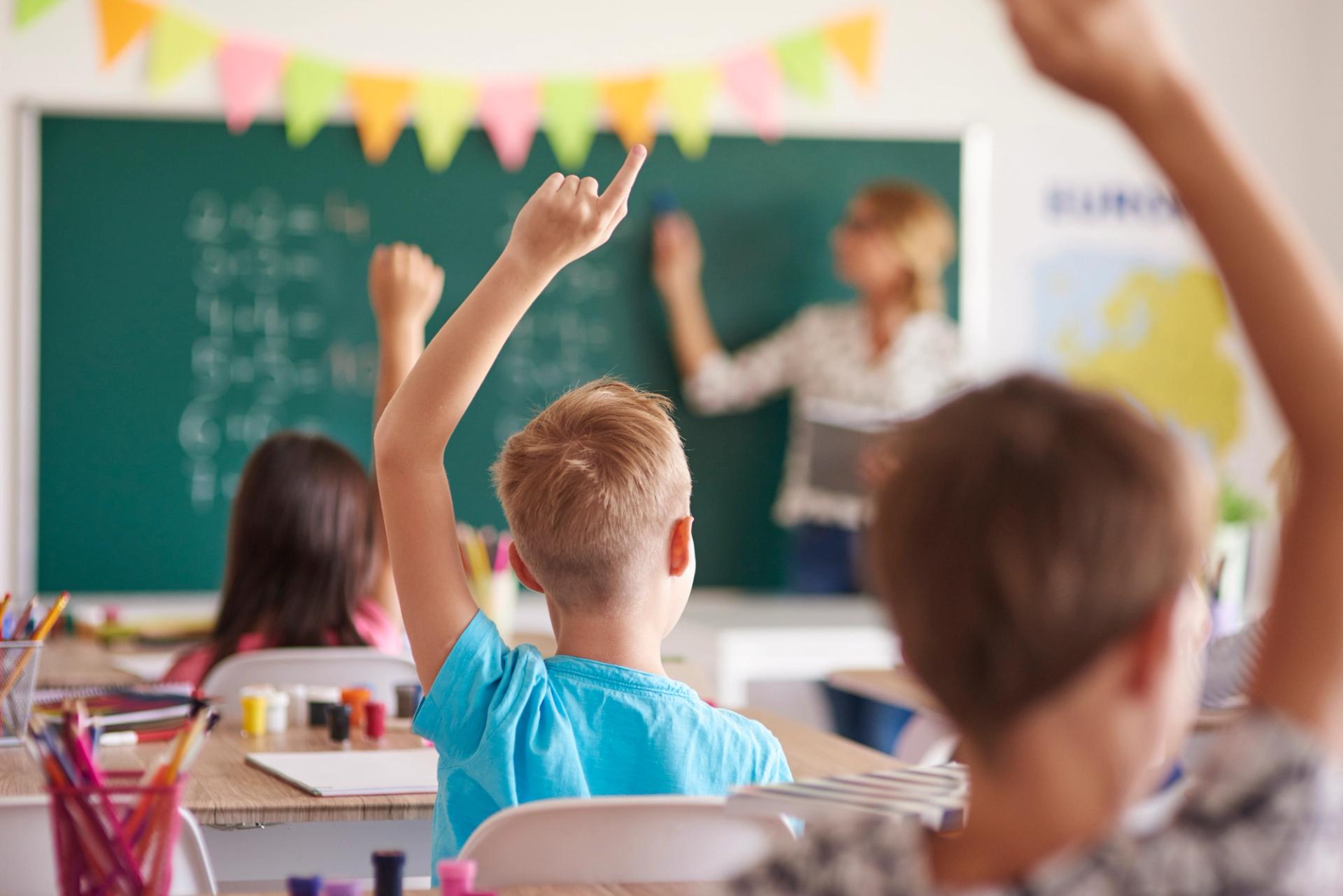 Two students in a classroom raising their hands.