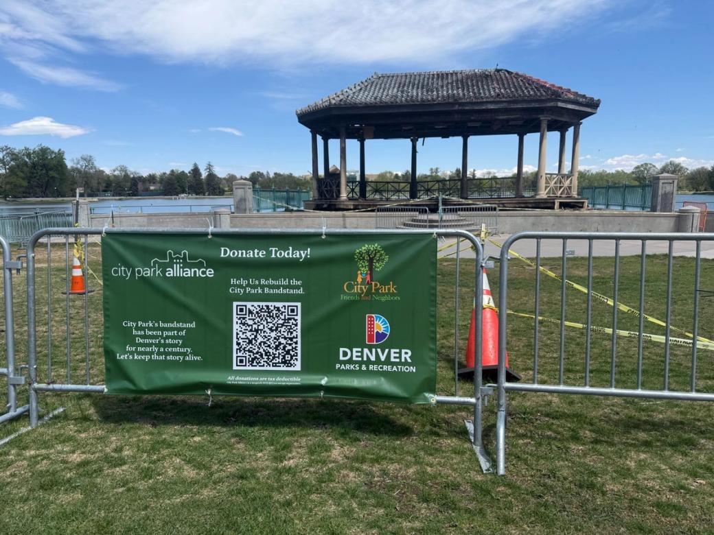A green banner on the barricade reads: City Park Alliance: Donate Today! Help us Rebuild the City Park Bandstand.