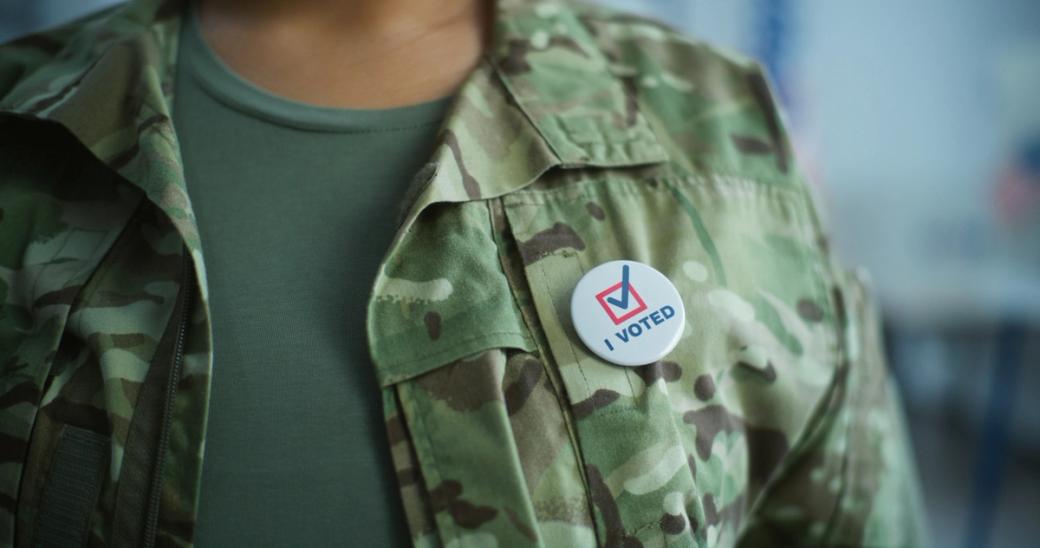 A person in a camouflage jacket is wearing an "I voted" button.