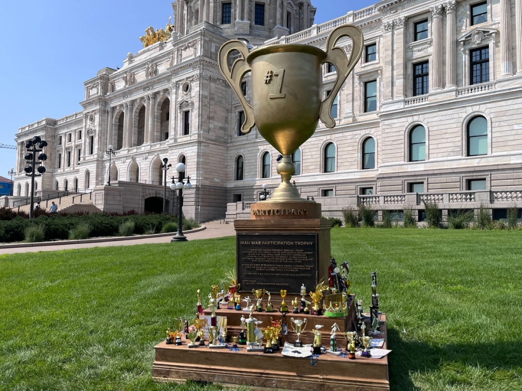 Large trophy with array of smaller trophies sits in the grass in front of Minnesota's capitol building