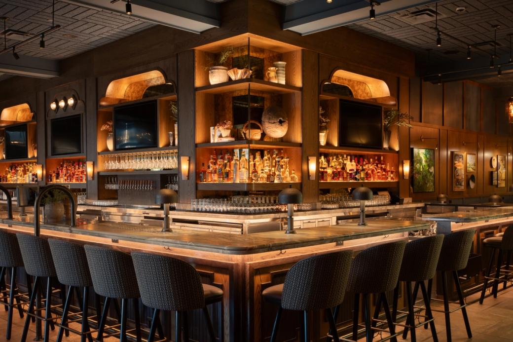 A bar with gray seating and walls, and shelves lit with orange lights.