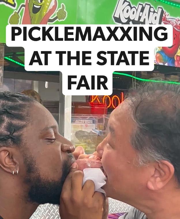 Two people take a bite of a pickle dog together.
