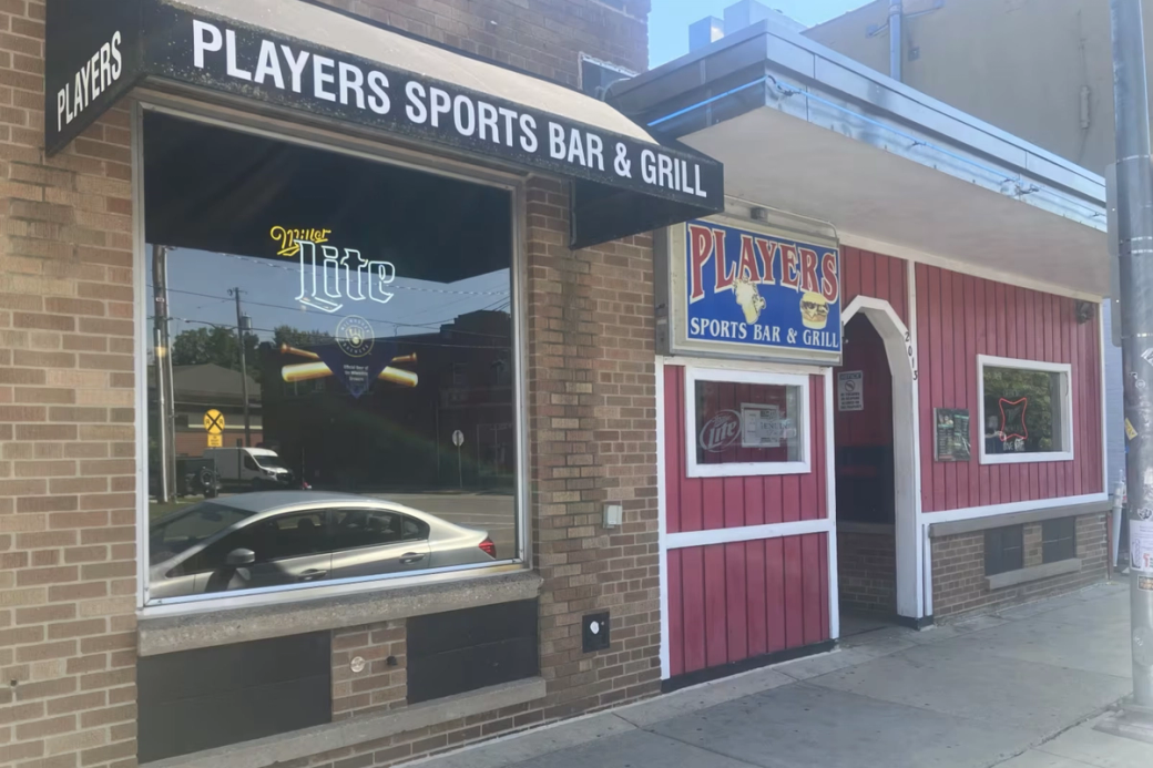The exterior of a bar with brick and red wood.