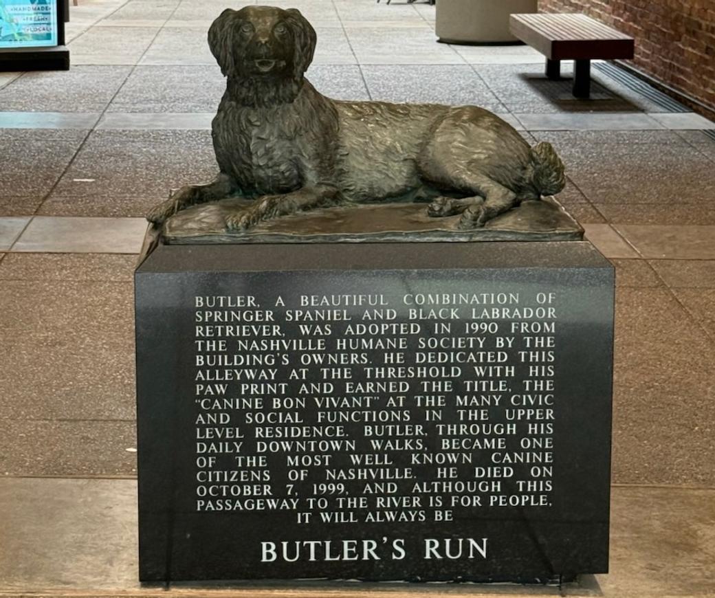 A dog statue on a sidewalk. A plaque says "Butler's Run," along with the story of the dog.