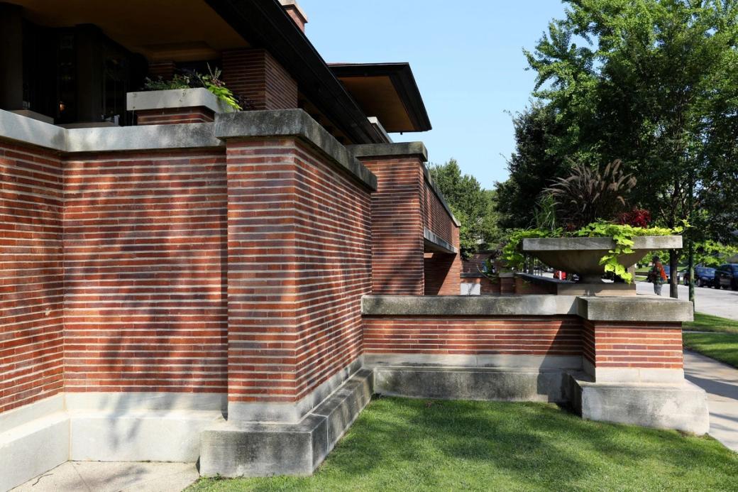 A side view of a red brick building. It is sunny out and the trees and grass are green