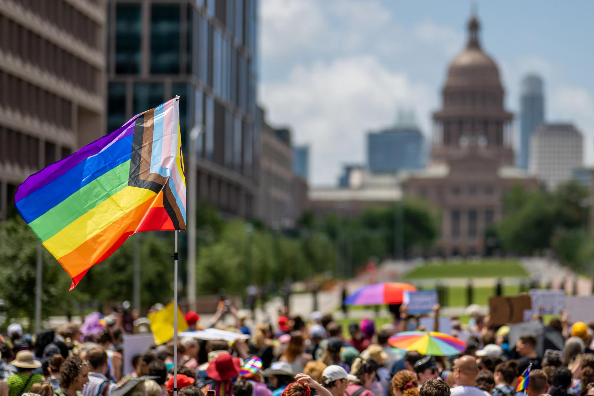 An image of a Pride flag being waved in a crowd outside the Texas Capitol.