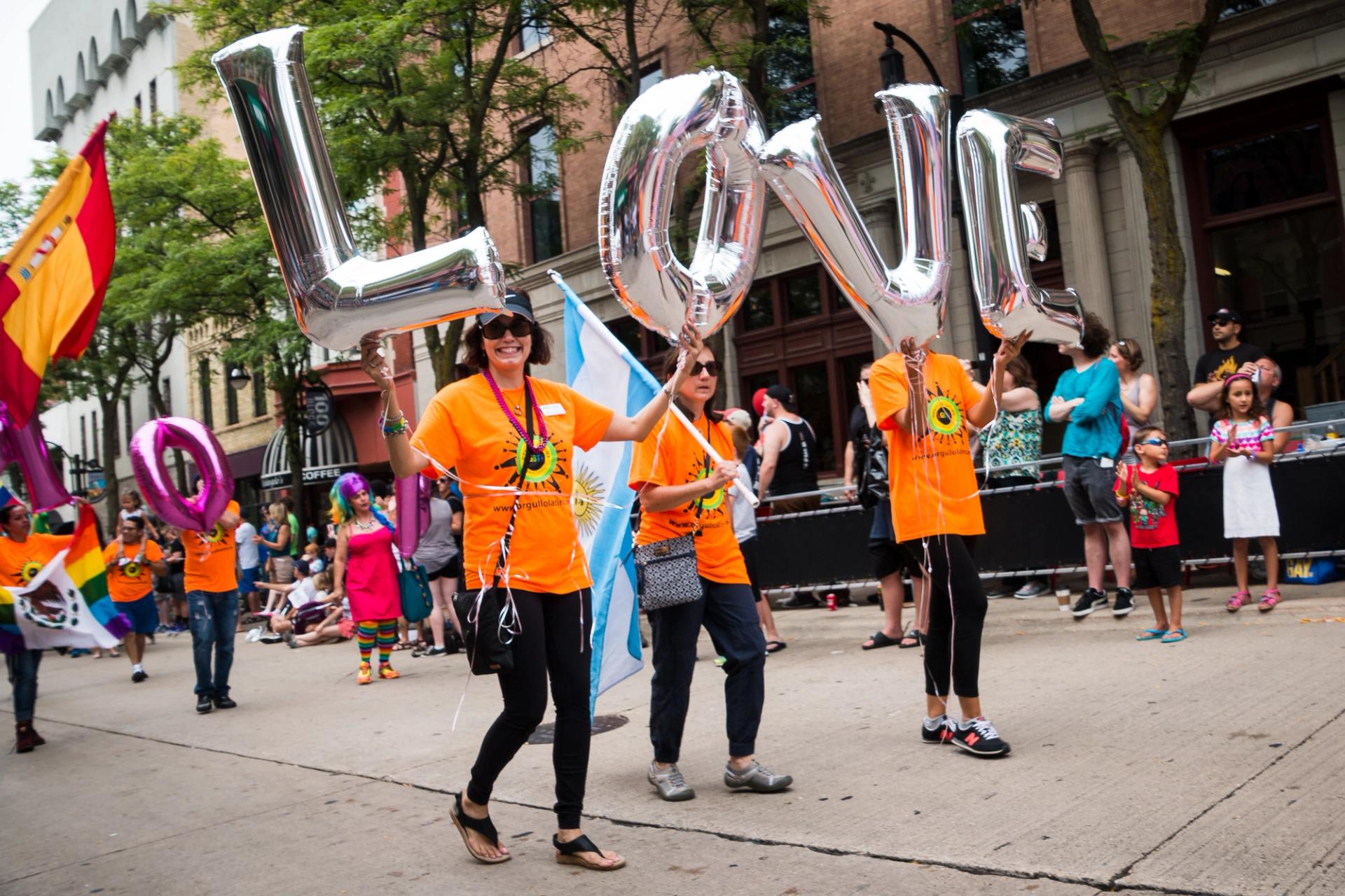 People in a Pride parade in Madison, holding silver balloon letters that spell "love."