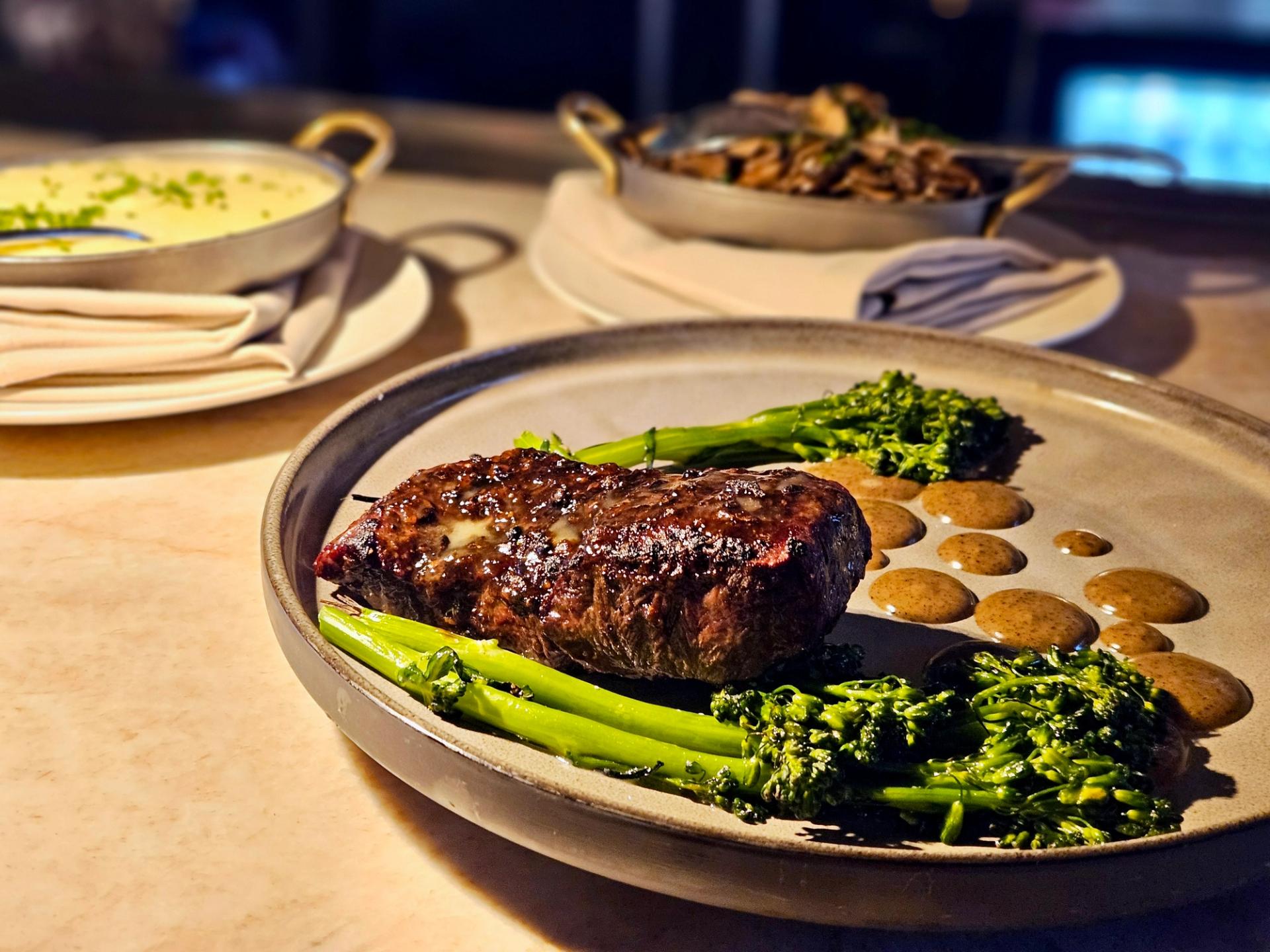 A steak with brocolli and side dishes in the background.