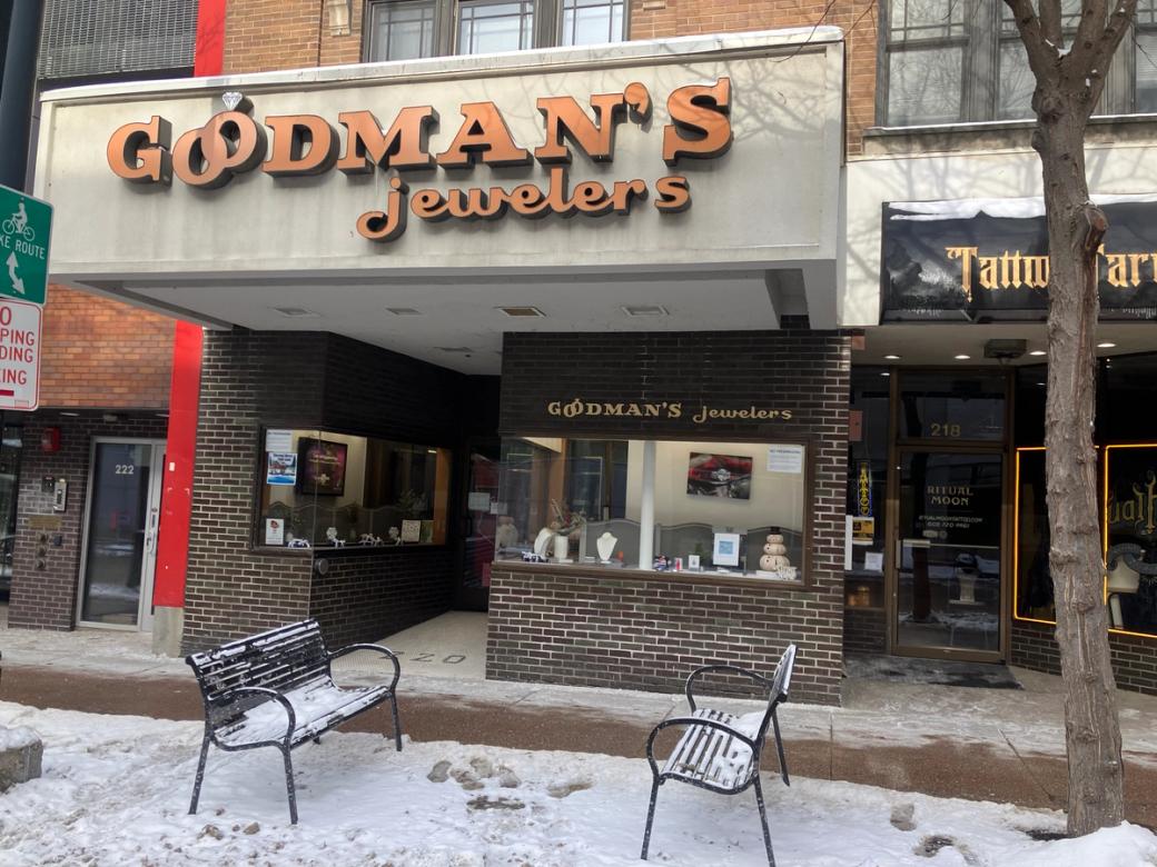 A storefront with two benches in front of it and snow on the ground.
