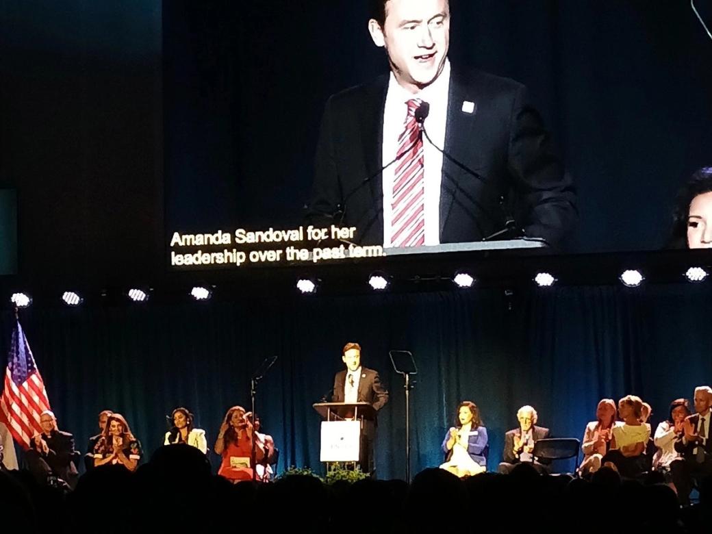 photo of Mayor Mike Johnston standing at a podium, his giant face on a screen behind him.