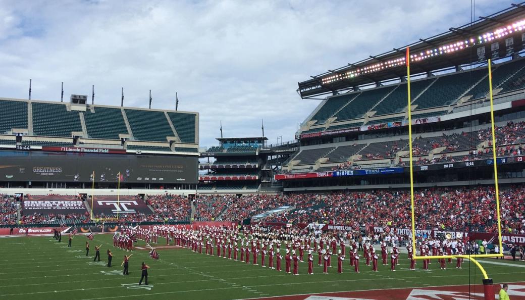 A marching band dressed in red and white uniforms performs in front of a crowd on the football field.
