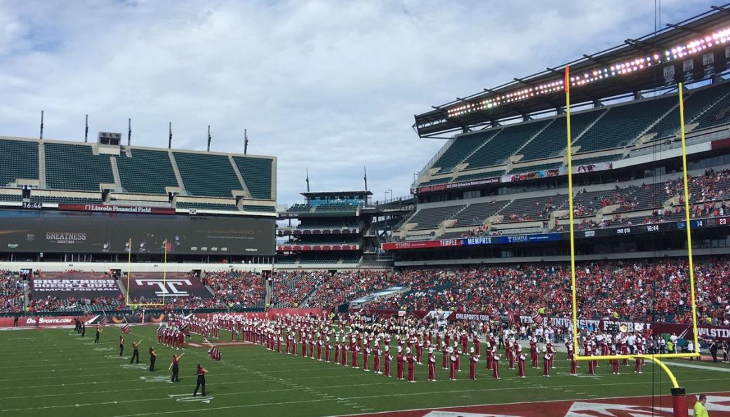 A marching band dressed in red and white uniforms performs in front of a crowd on the football field.