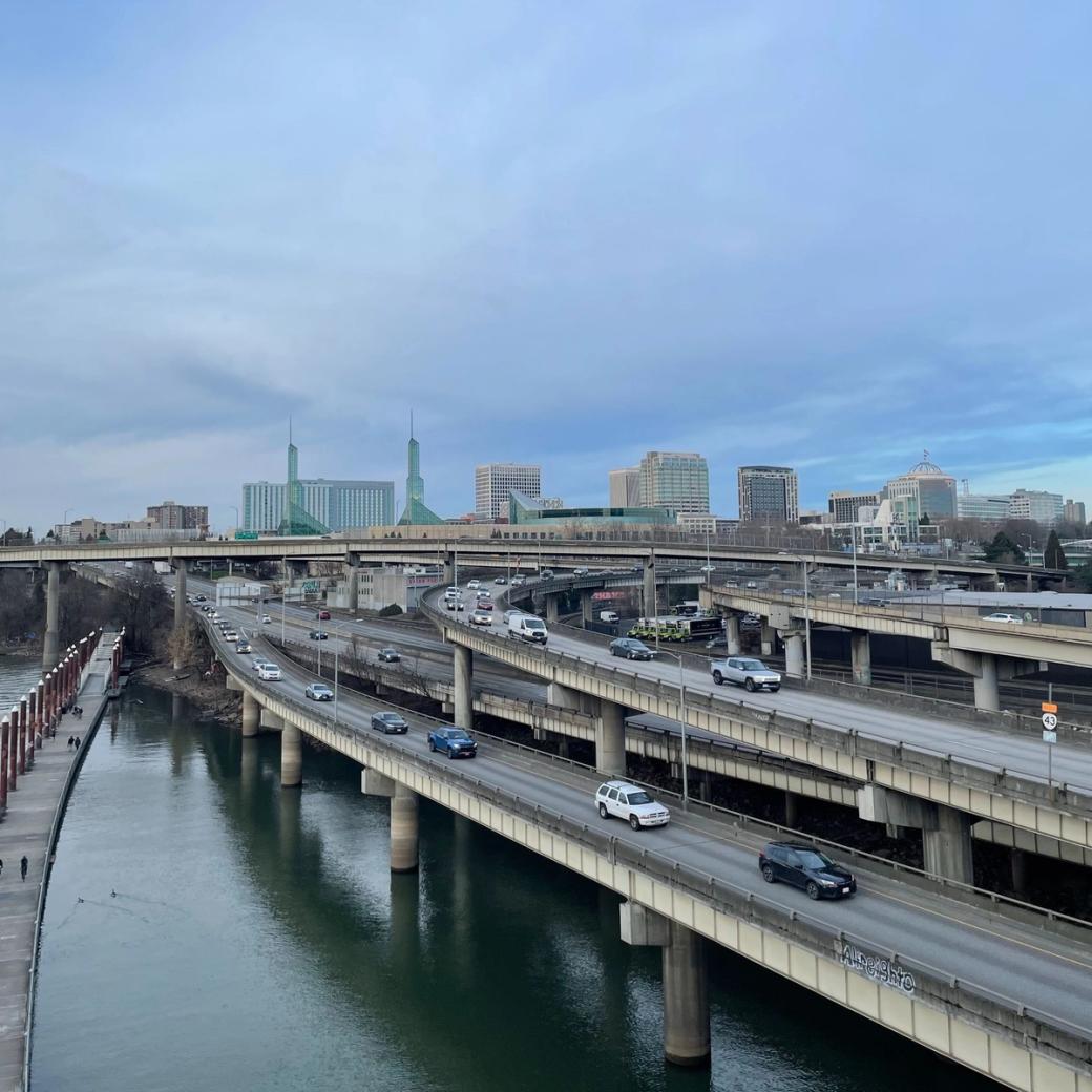 Cars driving in multiple lanes on a highway next to a river on a cloudy day.