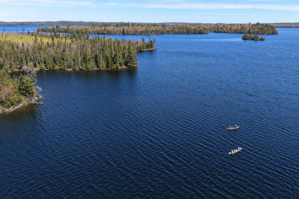A large blue lake in the boundary waters with multiple islands and two small canoes floating on the serene waters.
