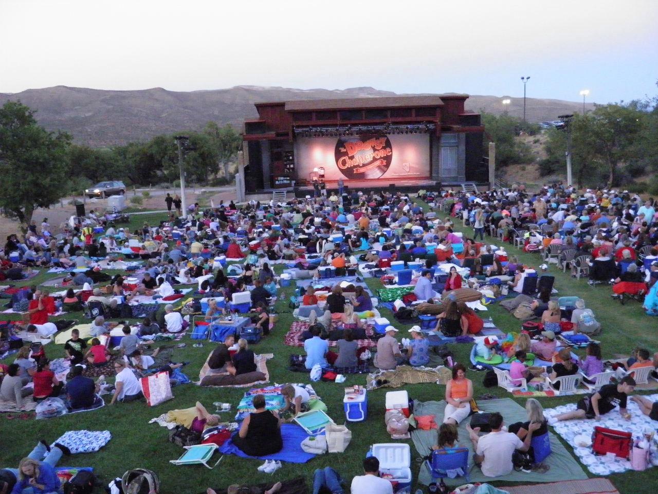 People sitting on blankets in front of an outdoor stage.