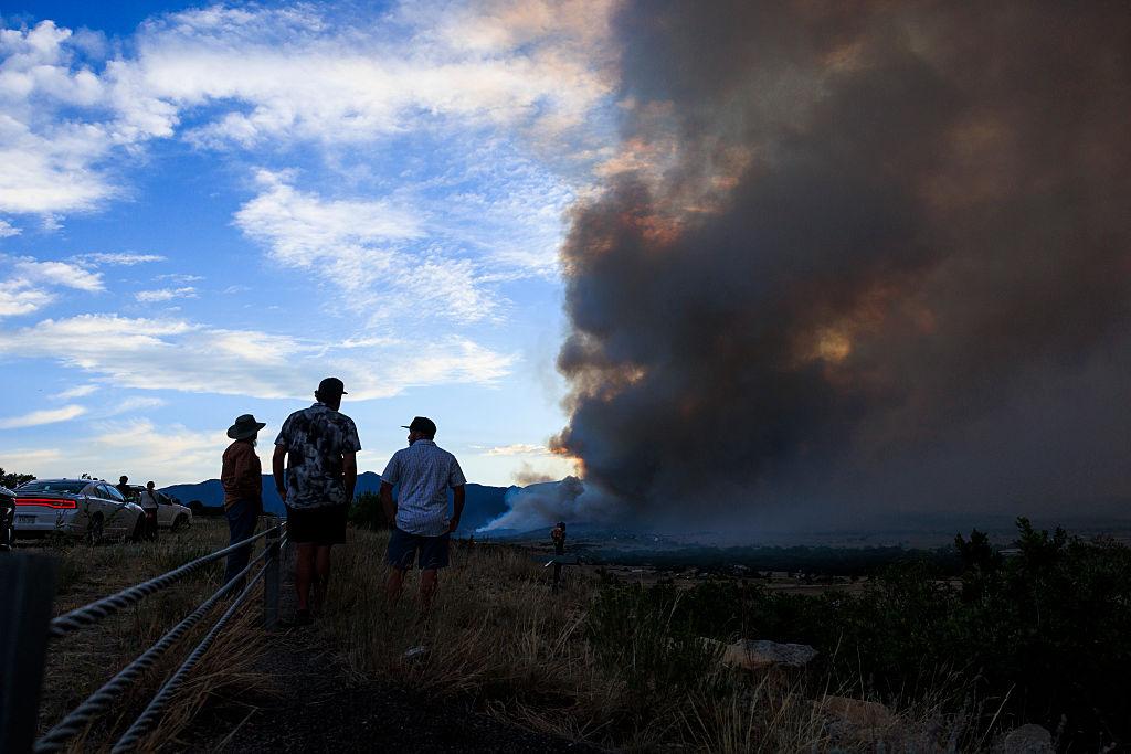 Wildfire burns in the background as three people look on
