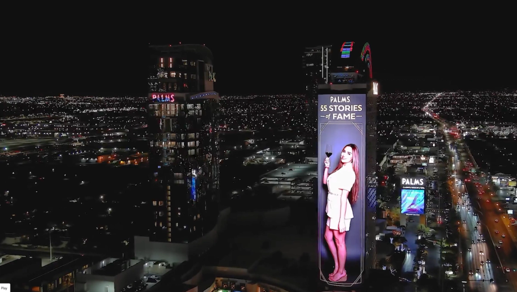 A skyscraper on the Strip shows a projection of a woman with a camera.