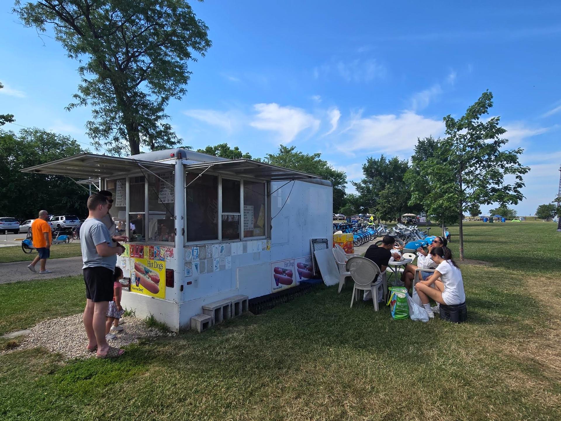 A group of people sitting outside of a hot dog shack
