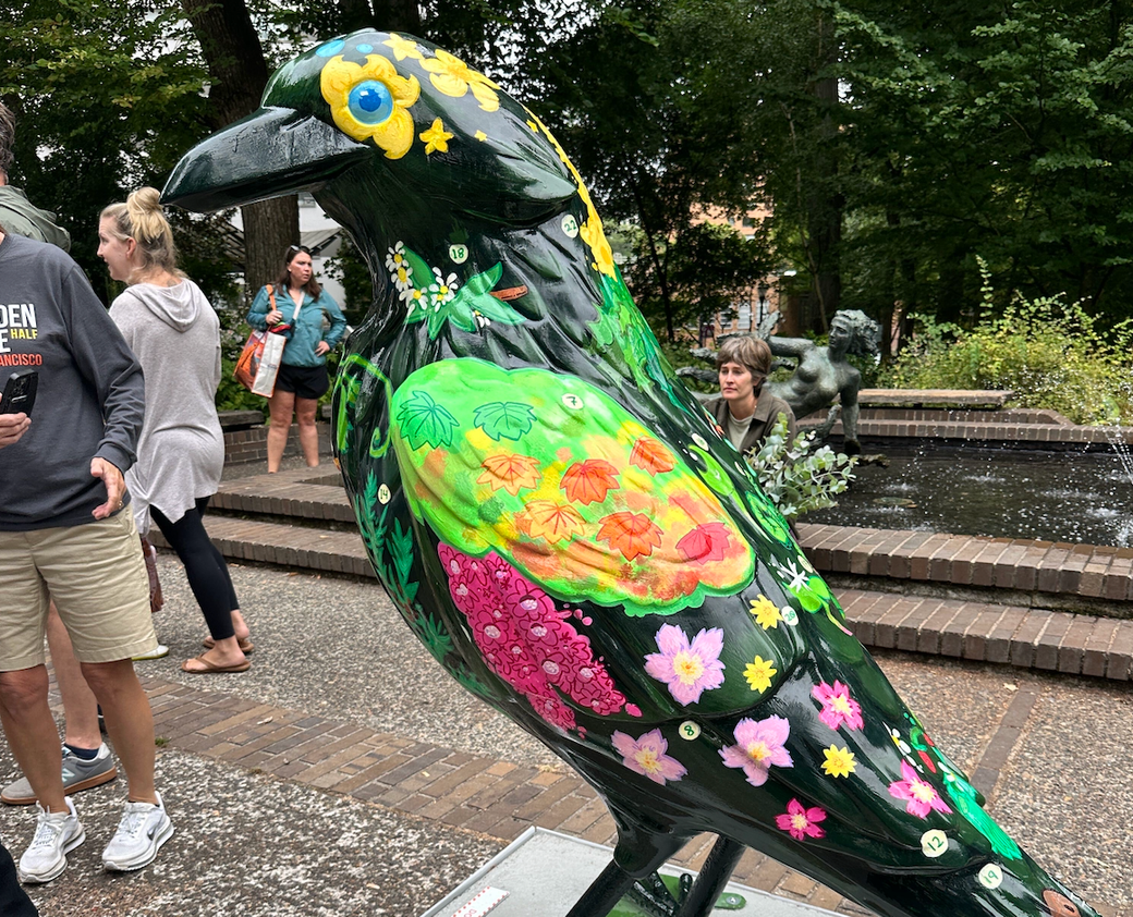 Large sculpture of crow with colorful array of flowers painted on it, and people milling in the background