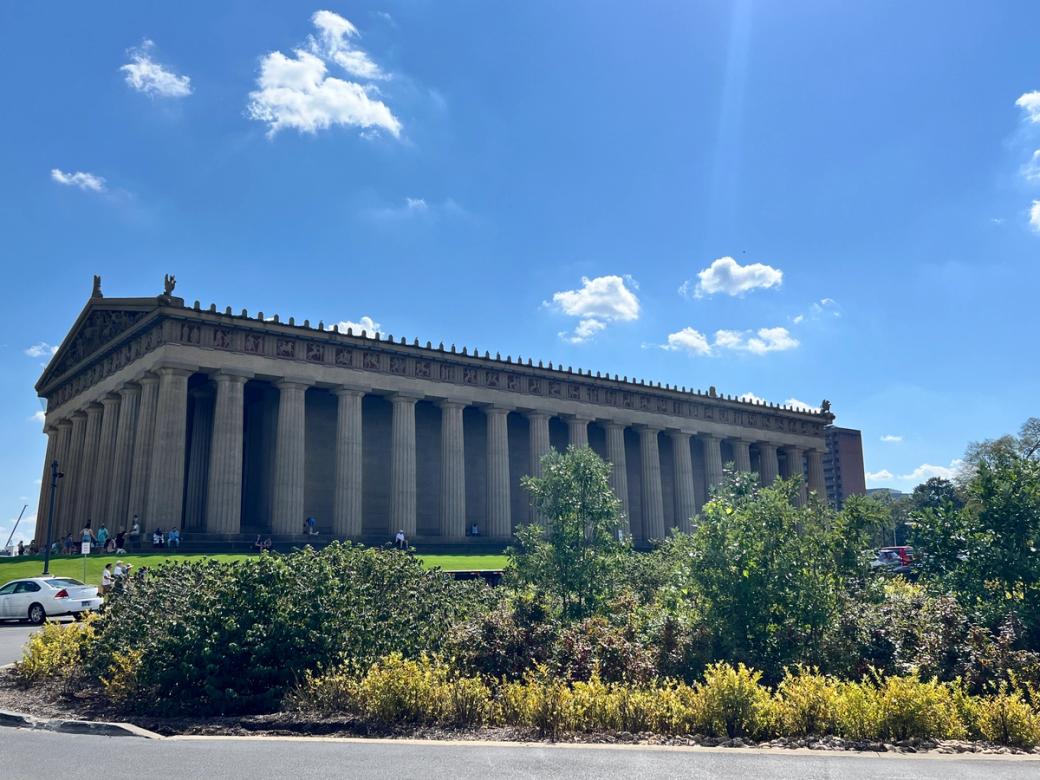 A replica of the Greek Parthenon surrounded by a garden. The sky is bright blue.