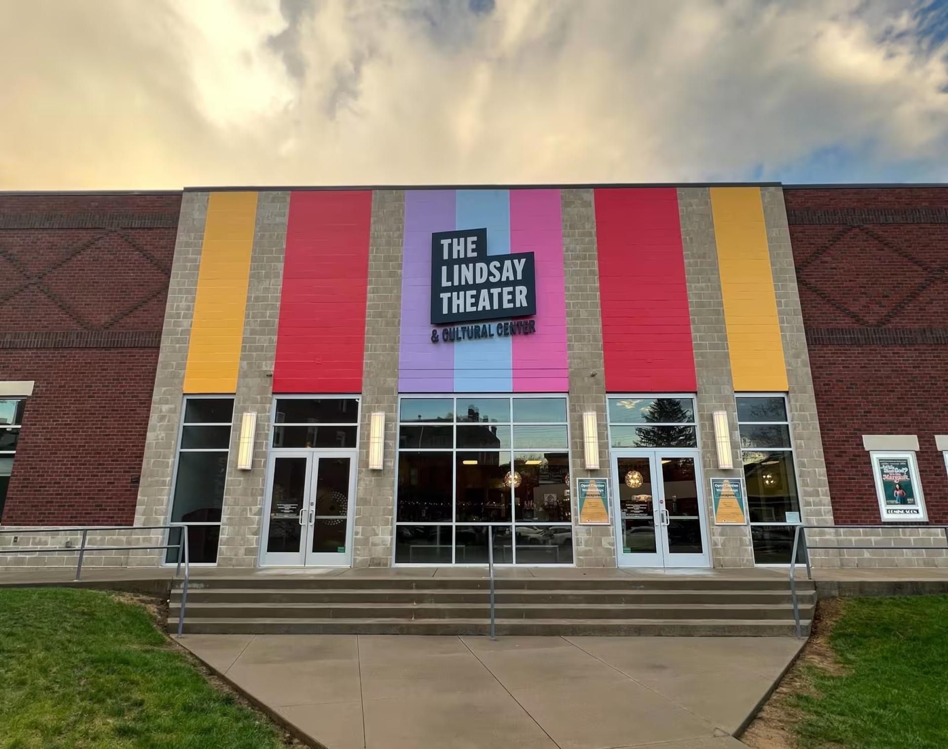 The front of The Lindsay Theater which has bright stripes along the front above its windows and glass doors. 