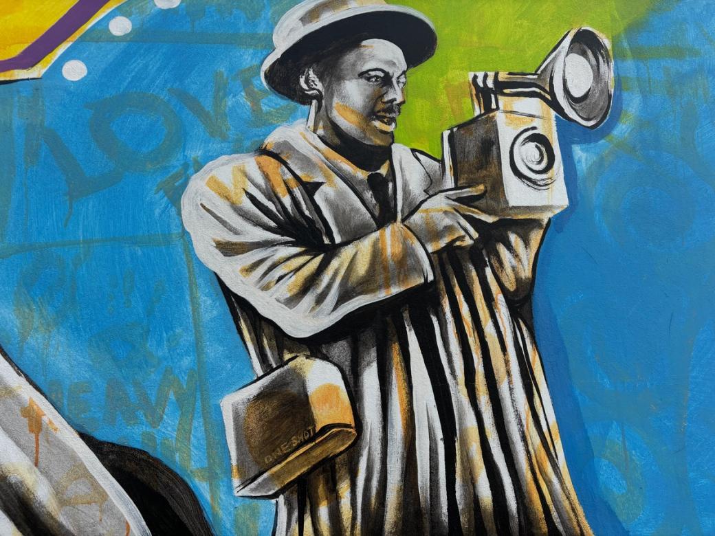 a mural of a Black photographer with an old camera and a fedora with a blue and green background