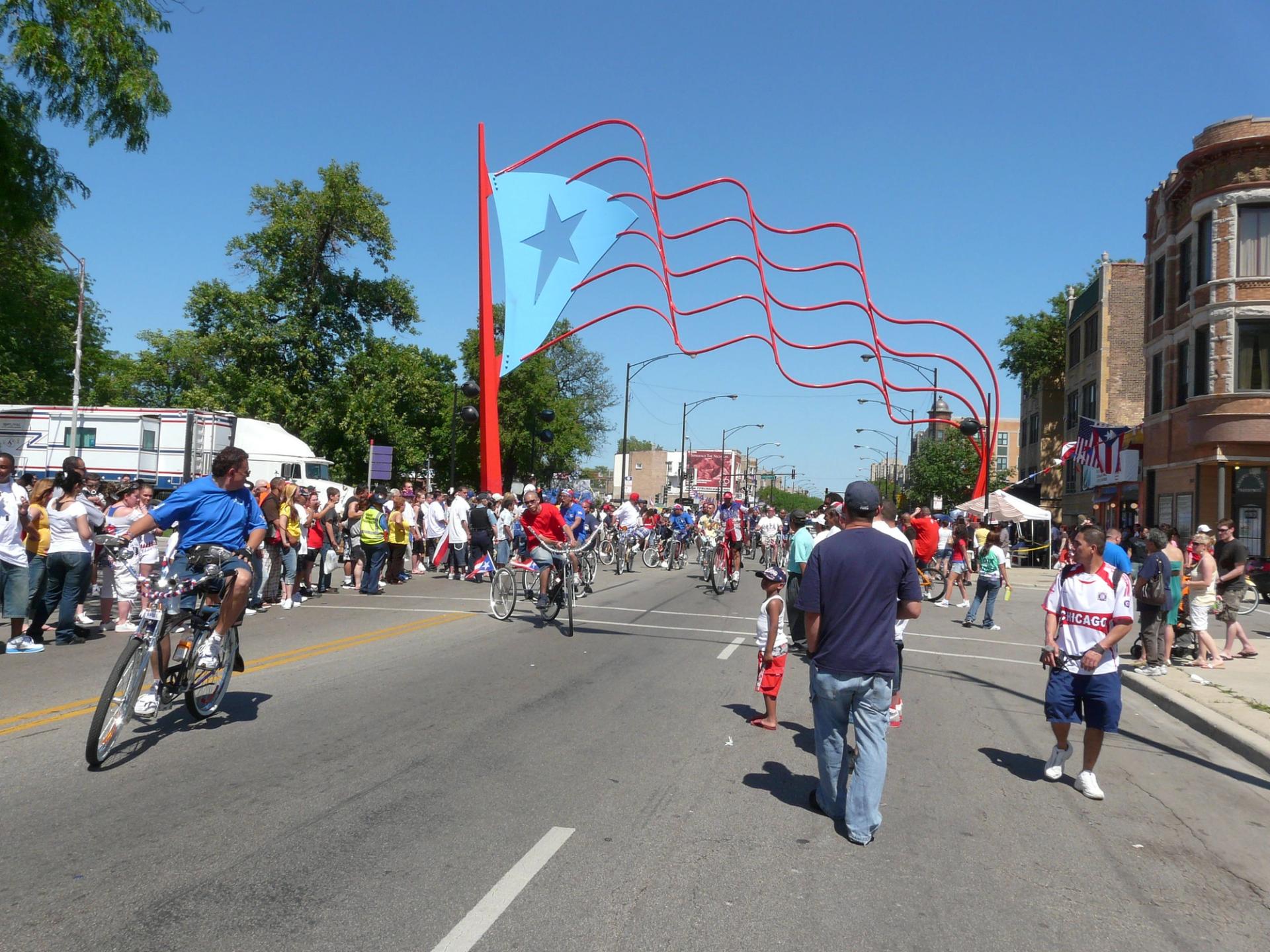 People walk down a street with a large sculpture of Puerto Rican flag in the distance