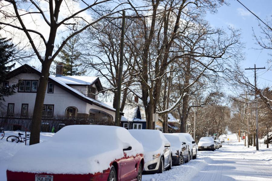 snow covered cars parked on one side of the street