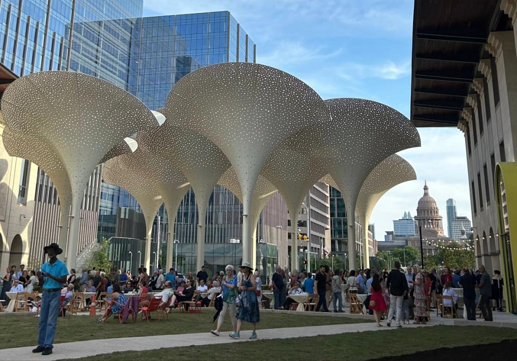 Large, white petal-like sculptures stand outside an art museum with the Texas Capitol in the background.