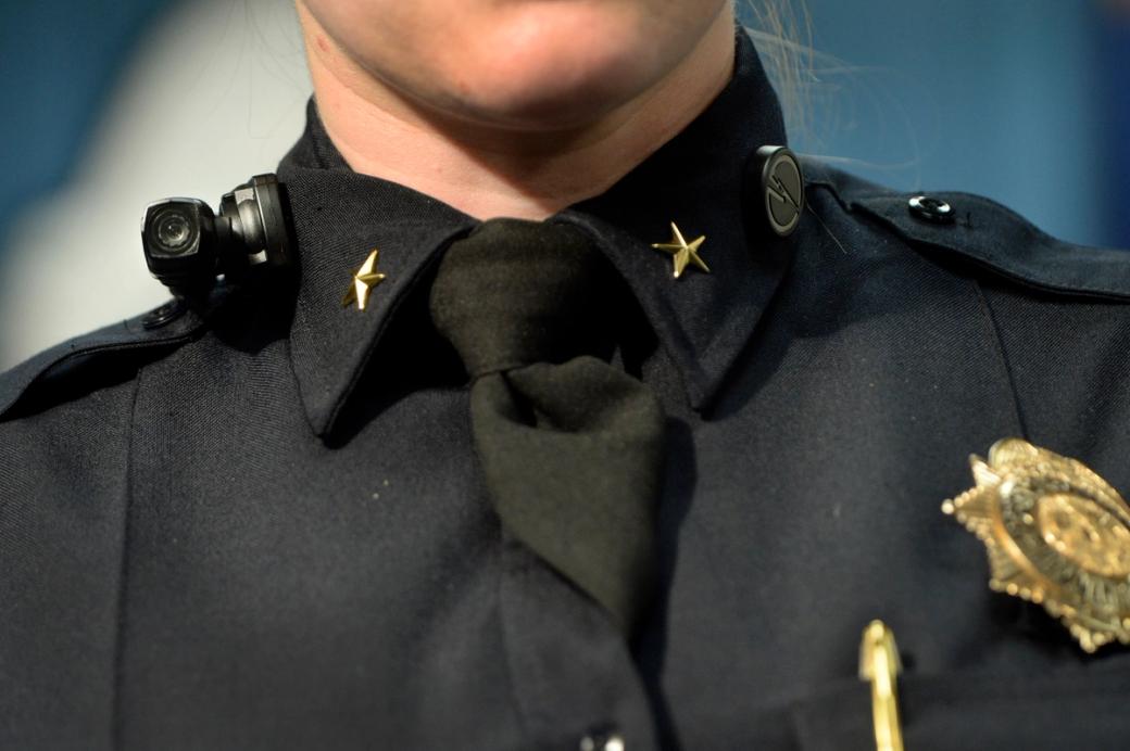 A police officer’s chin and shoulders in uniform with a body camera on her collar .