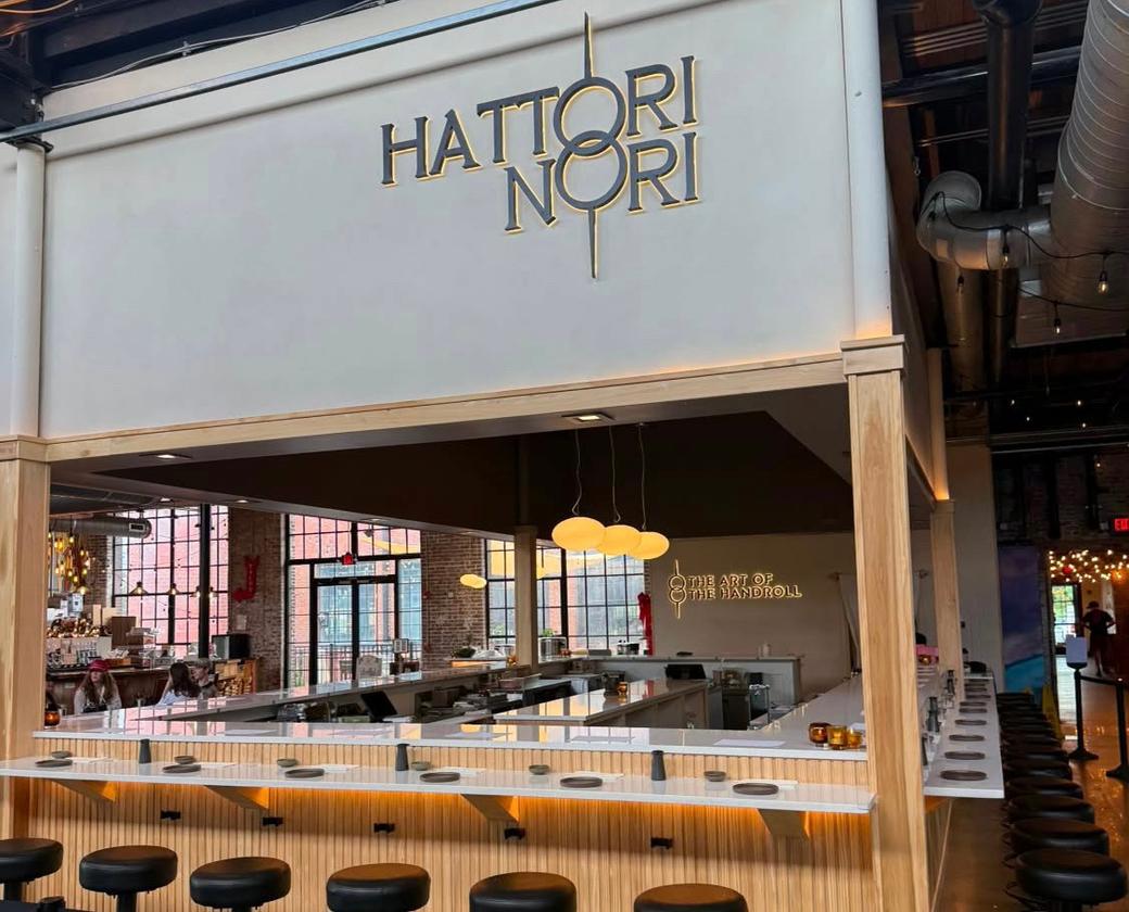 Stool seating at a wooden bar setup with white tables and a white top that says Hattori Nori.