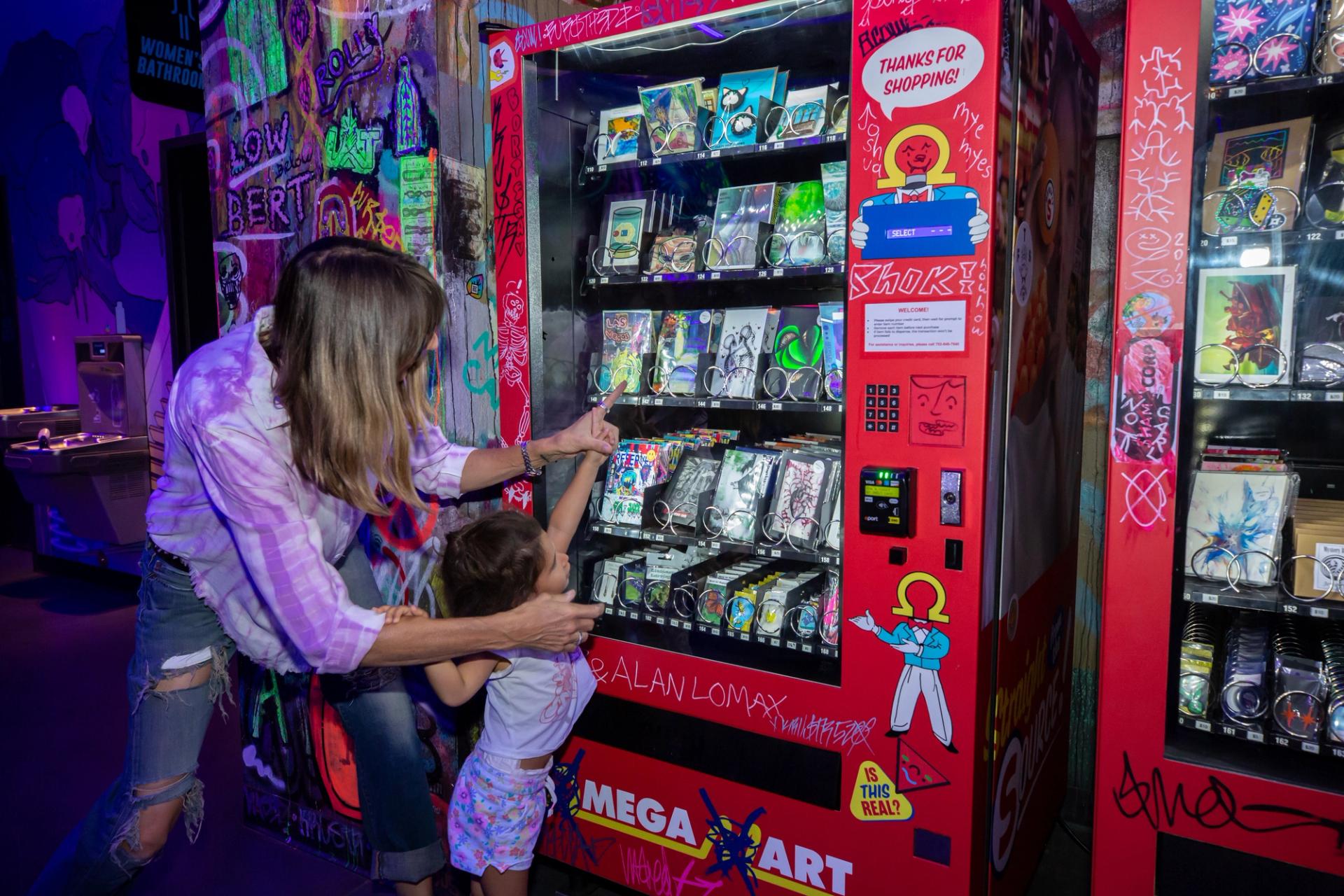 A mother and child buy art from an Omega Mart vending machine.