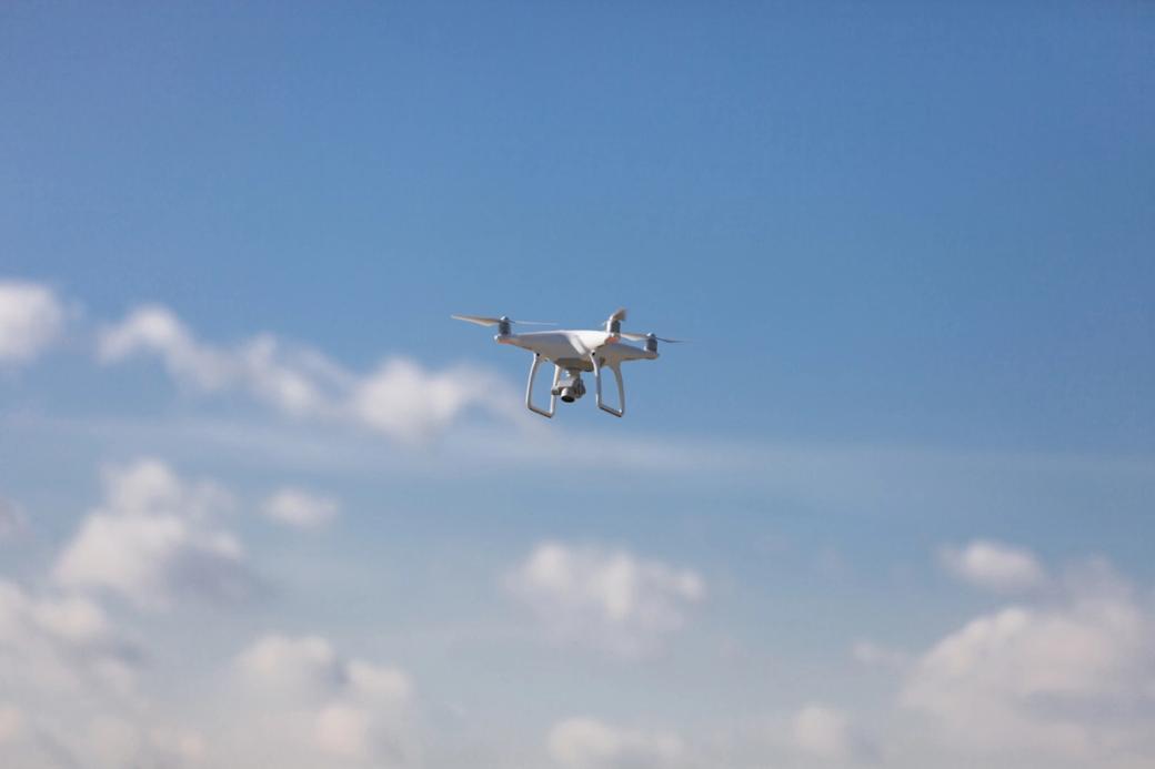 Quadcopter hovering against a blue sky with light clouds