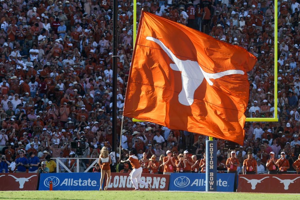 A large burnt orange flag with a white longhorn logo on it is flown across a football field.