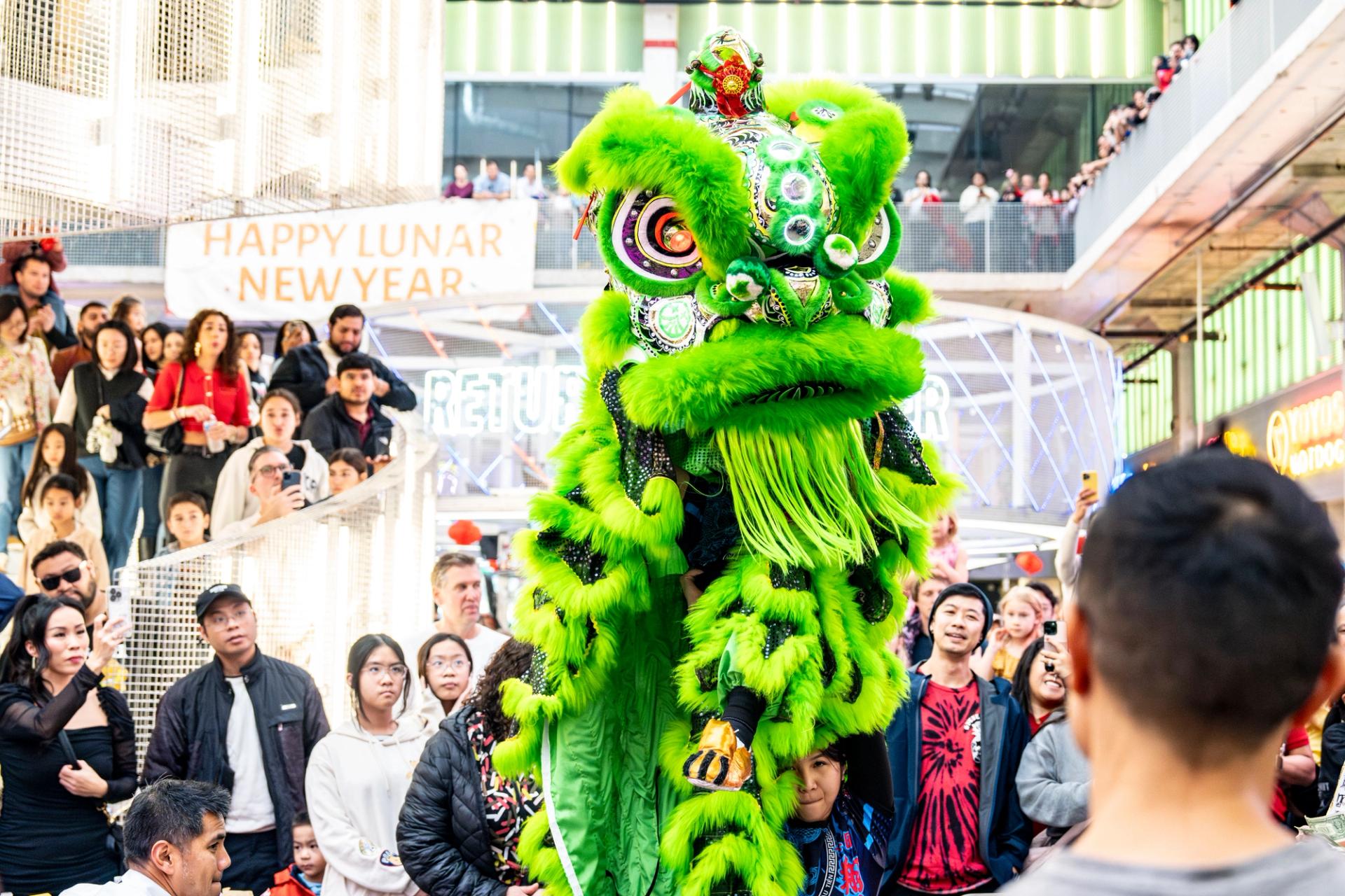 A bright green dragon-lion puppet is held up my people in a crowd in Houston for Lunar New Year.