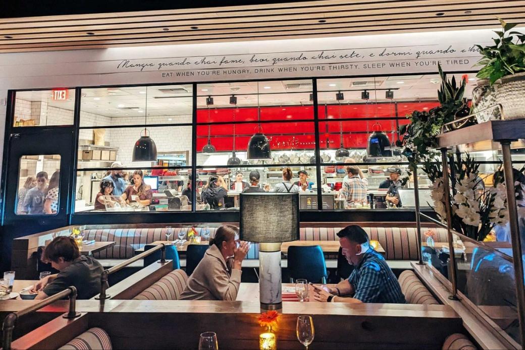 People eating at booths in a restaurant with a glassed-in kitchen at the rear.