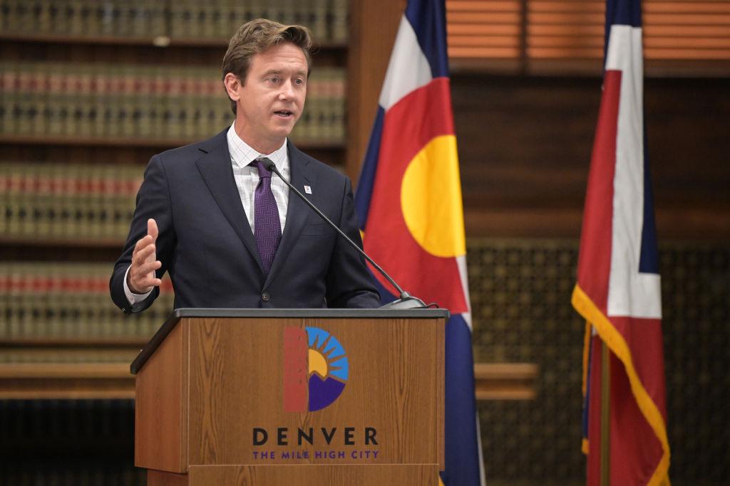 Mayor Mike Johnston speaks into a microphone at a podium that says “Denver The Mile High City.”