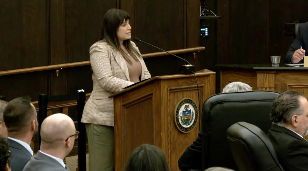  Allegheny County Executive Sara Innamorato stands at a lectern and addresses a crowd, speaking into a microphone.