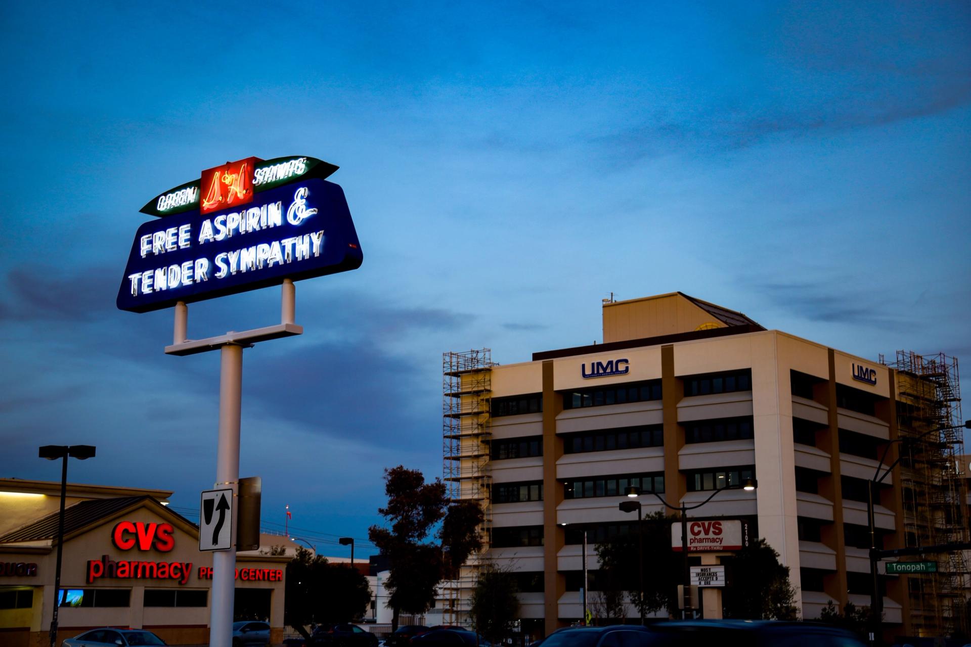A neon sign above a hospital and drug store.