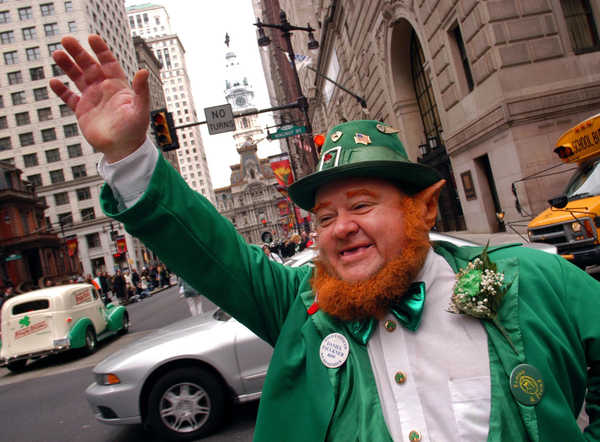 A man dressed as a leprechaun waves off camera
