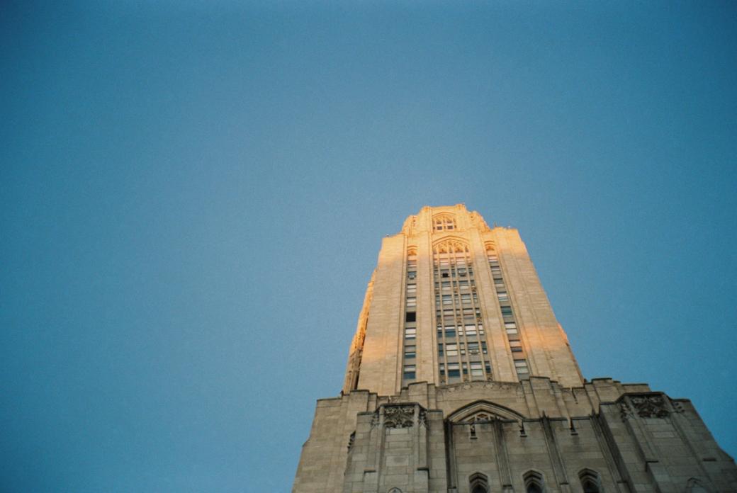 A gothic-styled stone building stretches up to a cloudless sky, with sunlight hitting the upper floors.
