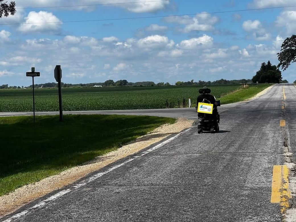 A wheelchair drives down an open road under blue skies.