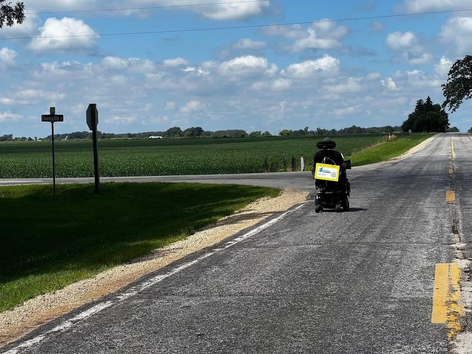 A wheelchair drives down an open road under blue skies.