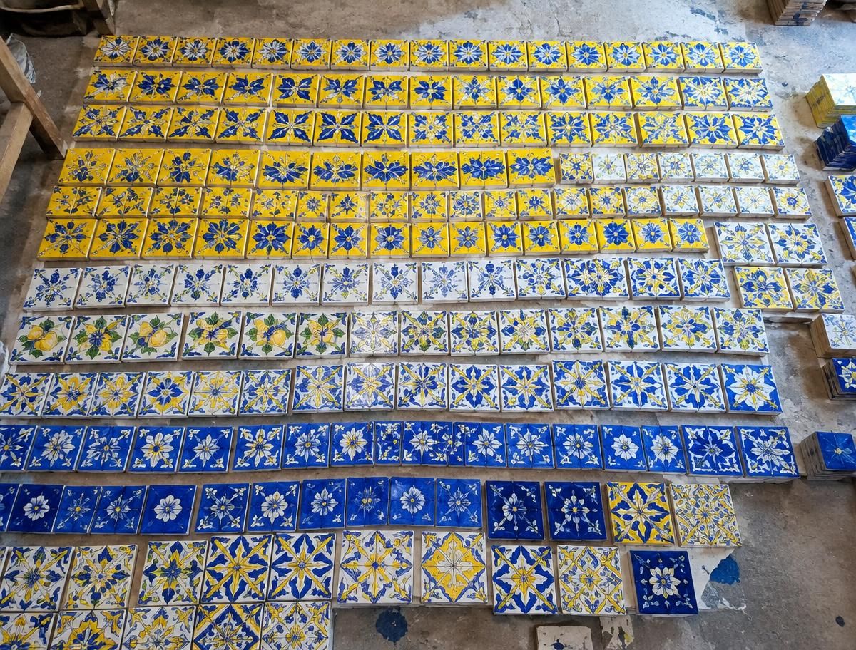 Hundreds of blue and yellow hand-painted ceramic tiles laid out in rows on a workshop floor