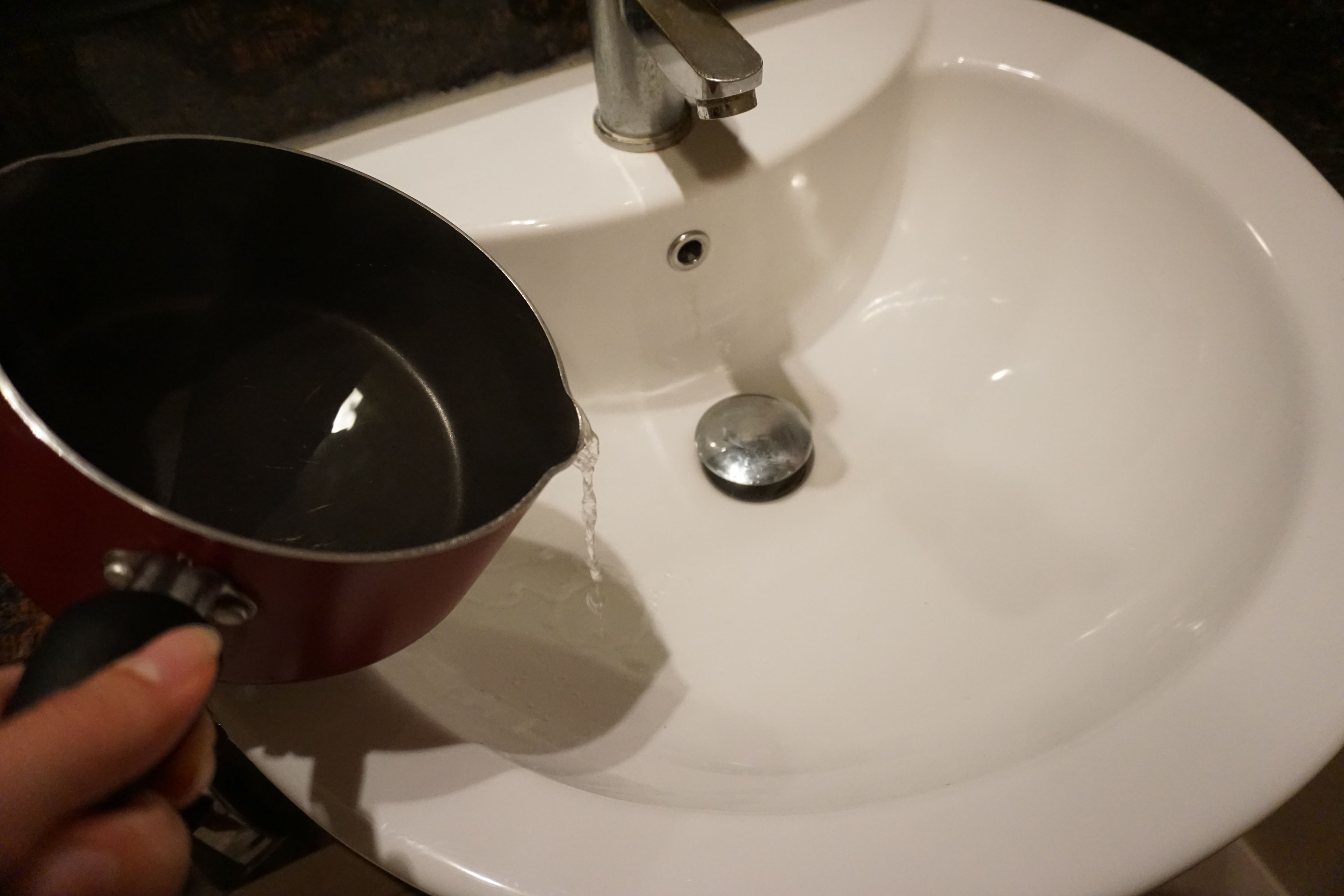 Bilde av en person som heller i en liter kokende vann i vasken for å åpne en tett vask