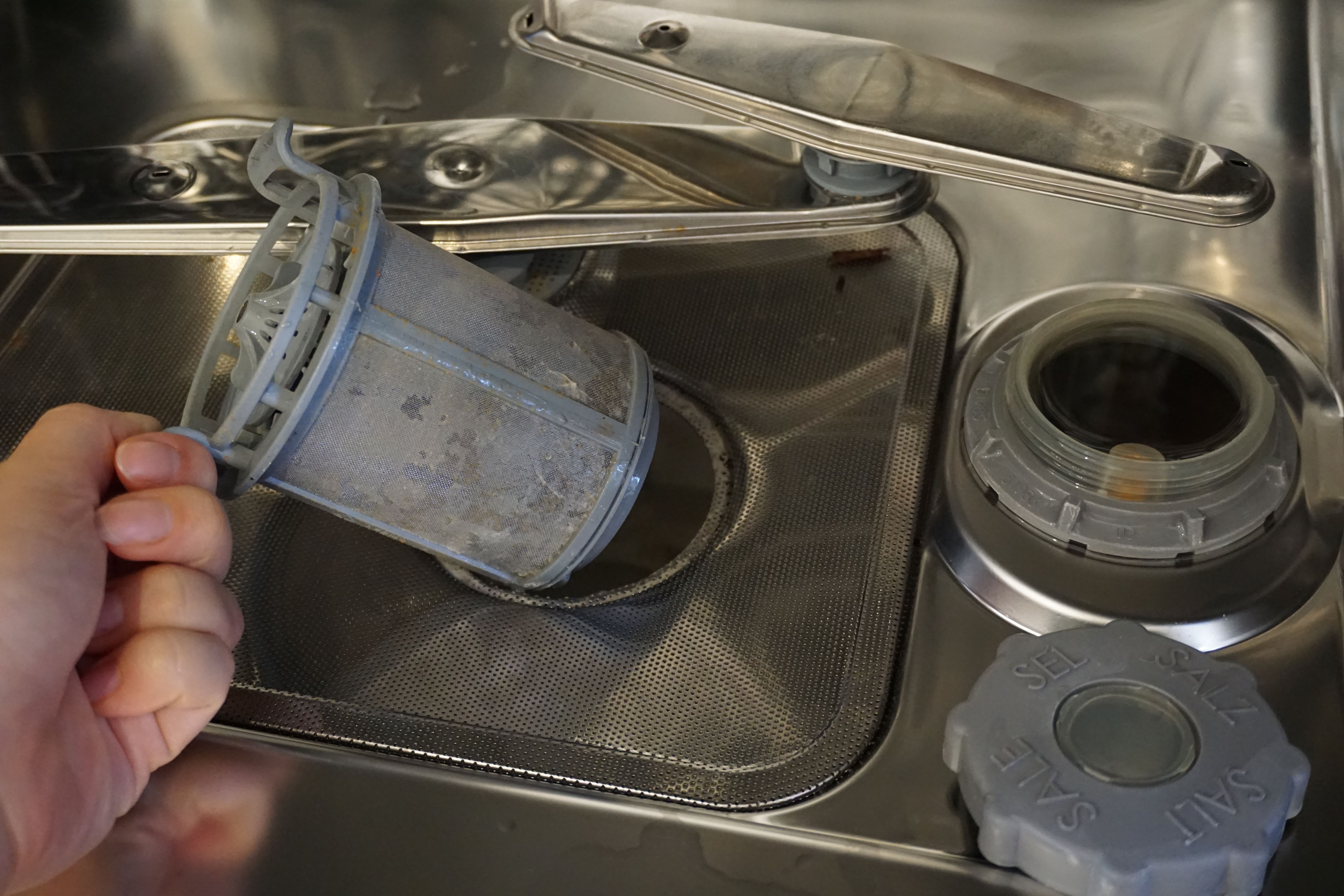 et bilde av et skittent filter Et bilde av en hånd som drar ut et skittent filter i oppvaskmaskinen