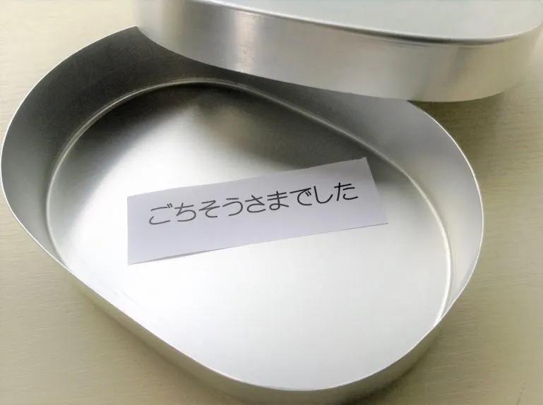An empty metal lunchbox or bento which has a paper inside which says ごちそうさまでした which is the Japanese word used when you are done eating