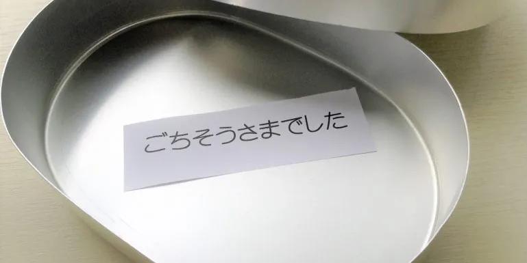 An empty metal lunchbox or bento which has a paper inside which says ごちそうさまでした which is the Japanese word used when you are done eating