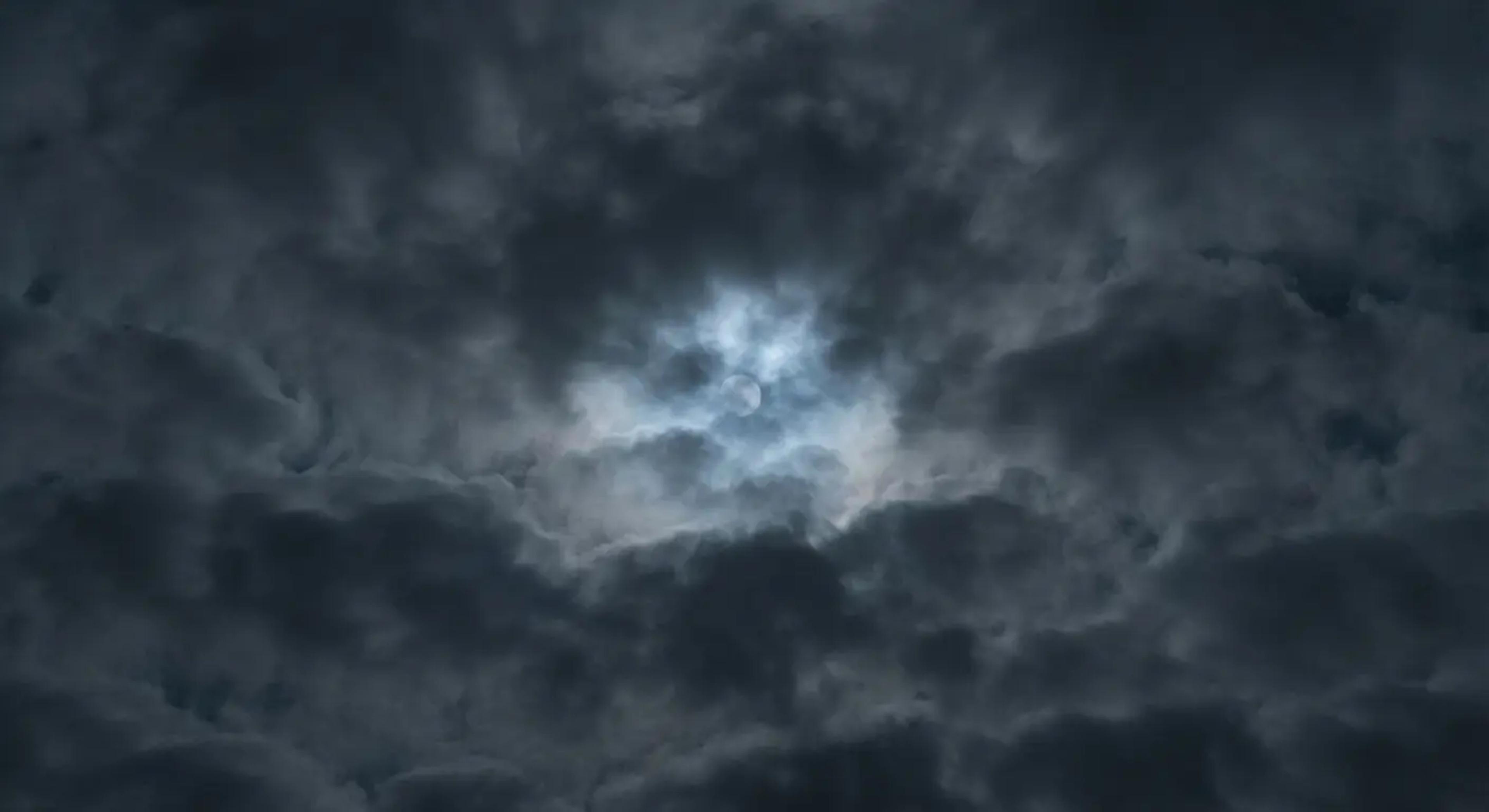 A glowing full moon faintly visible behind dense, dark night clouds, illustrating the Japanese aesthetic concept of Ugetsu (rainy moon) or Mugetsu (cloud-covered moon).