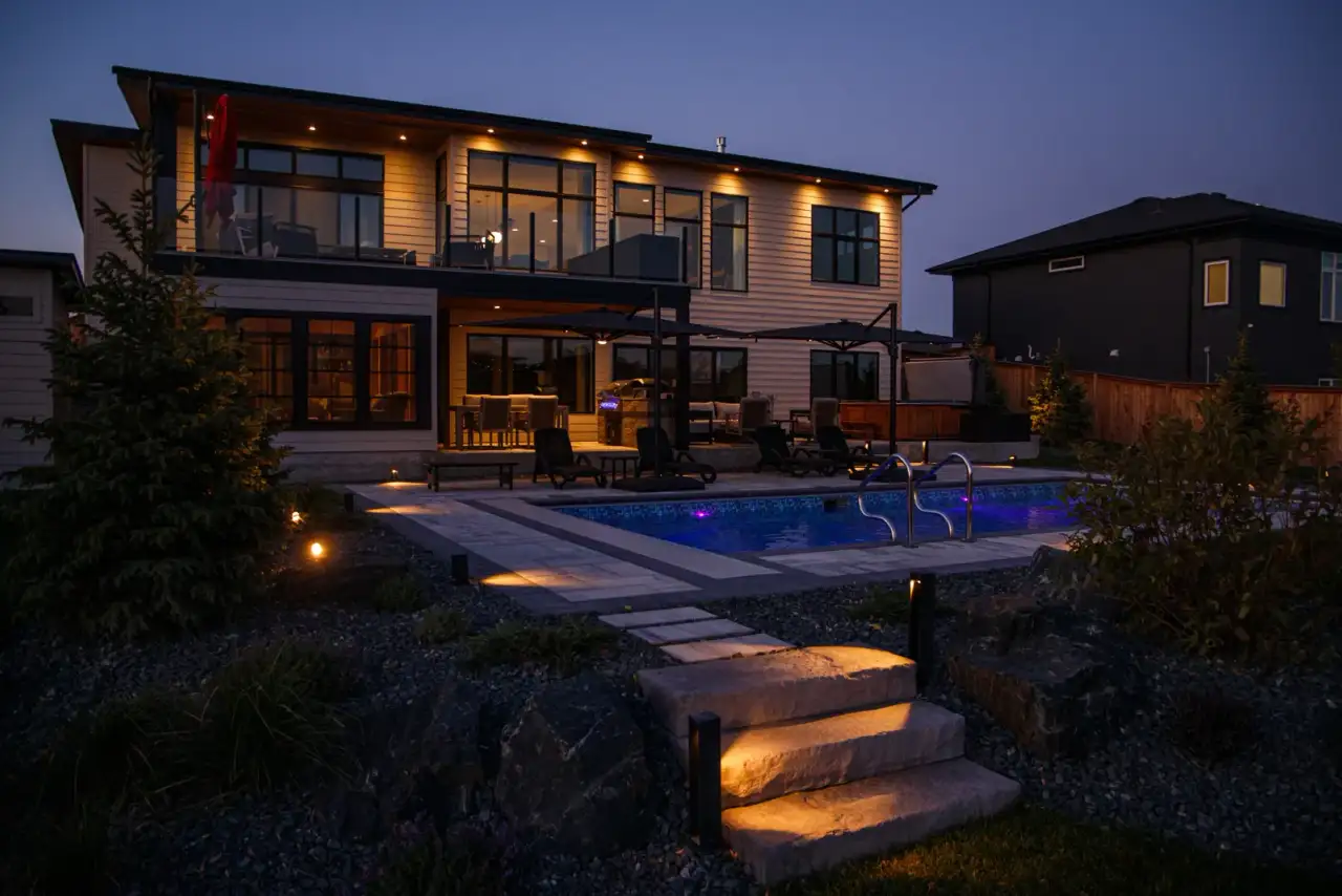 Modern house and backyard pool with landscape lighting at dusk
